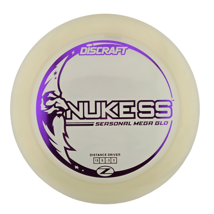 A Discraft Nukess Seasonal Mega Glo distance driver disc golf disc, featuring a translucent off-white plastic body with a purple and black printed graphic on a white background.